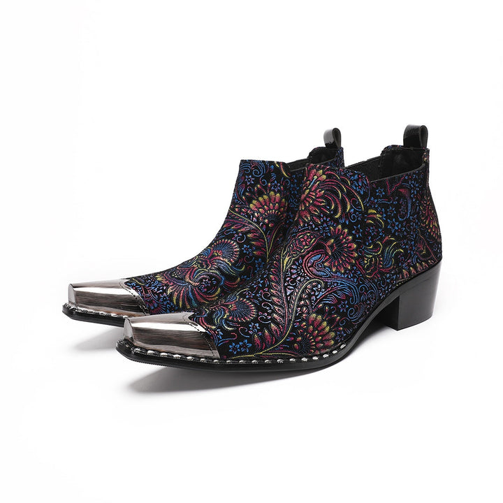 A pair of men's black ankle boots with a vibrant multicolor brocade pattern and a polished silver metal toe cap.