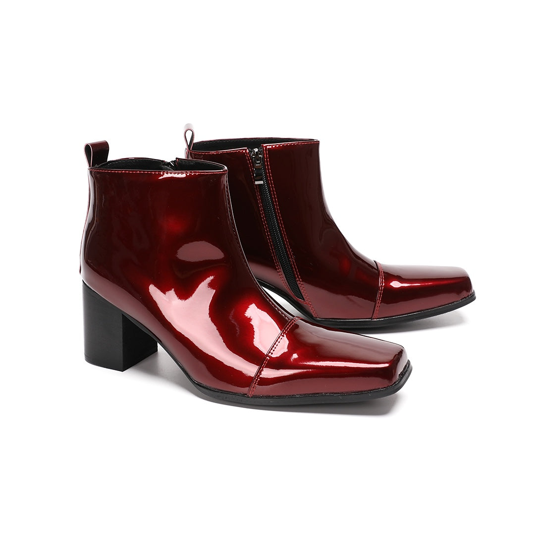 A pair of shiny burgundy patent leather ankle boots with a square toe and block heel, featuring a side zipper closure.
