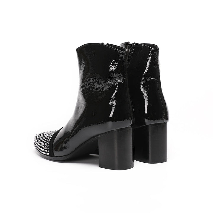 A pair of black patent leather ankle boots with rhinestone-embellished pointed toes and block heels.