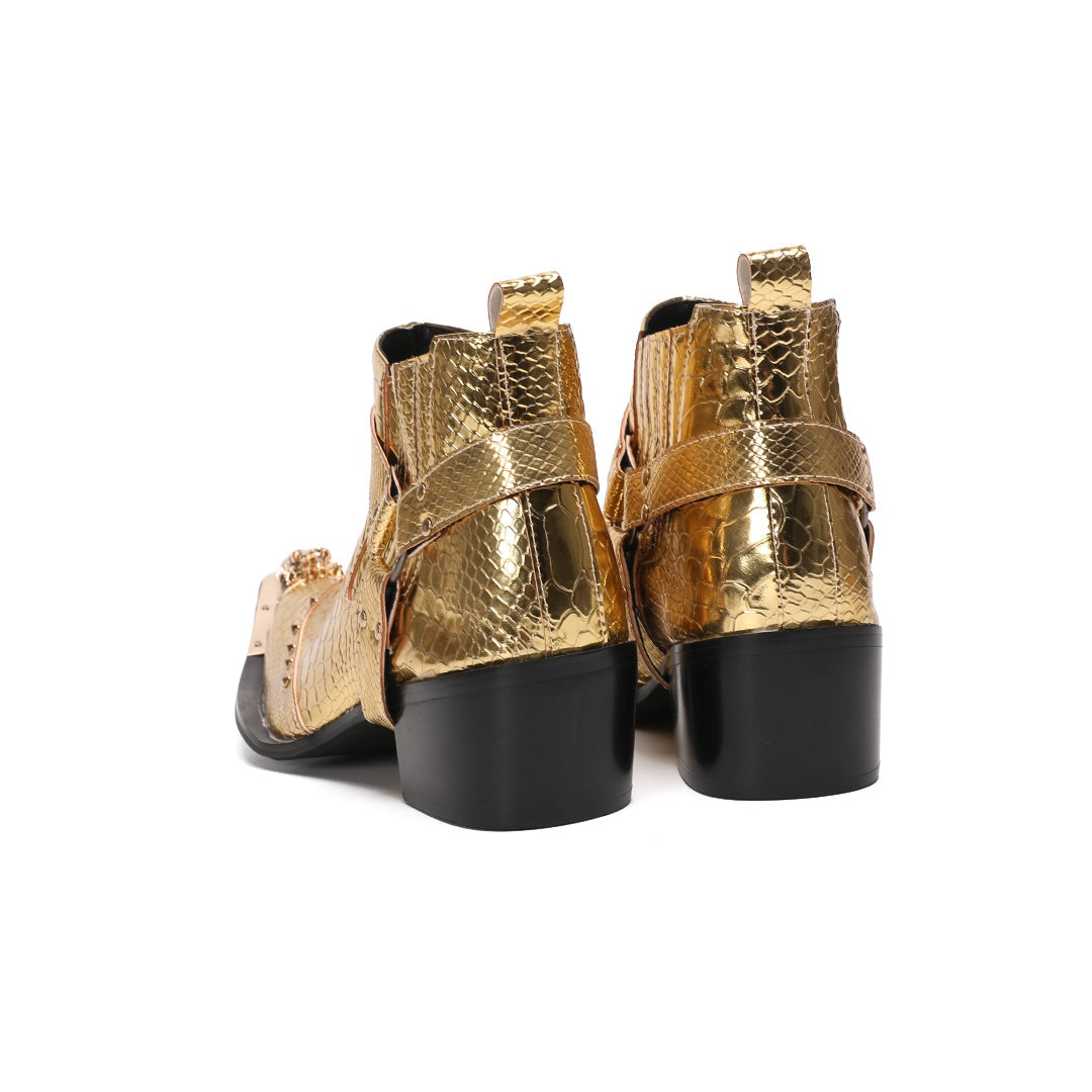 A pair of shiny gold snake skin textured ankle boots with a pointed metal toe cap, studded details, and an ankle strap.