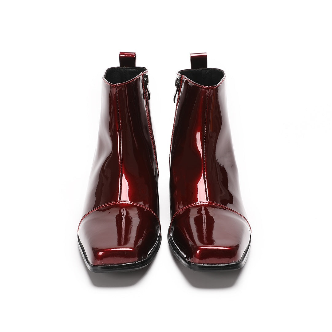 A pair of shiny burgundy patent leather ankle boots with a square toe and block heel, featuring a side zipper closure.