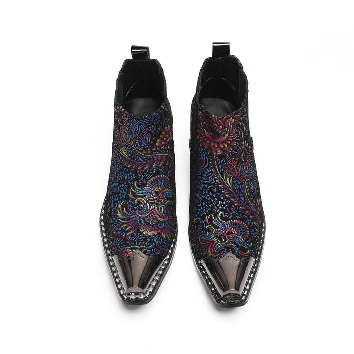 A pair of men's black ankle boots with a vibrant multicolor brocade pattern and a polished silver metal toe cap.