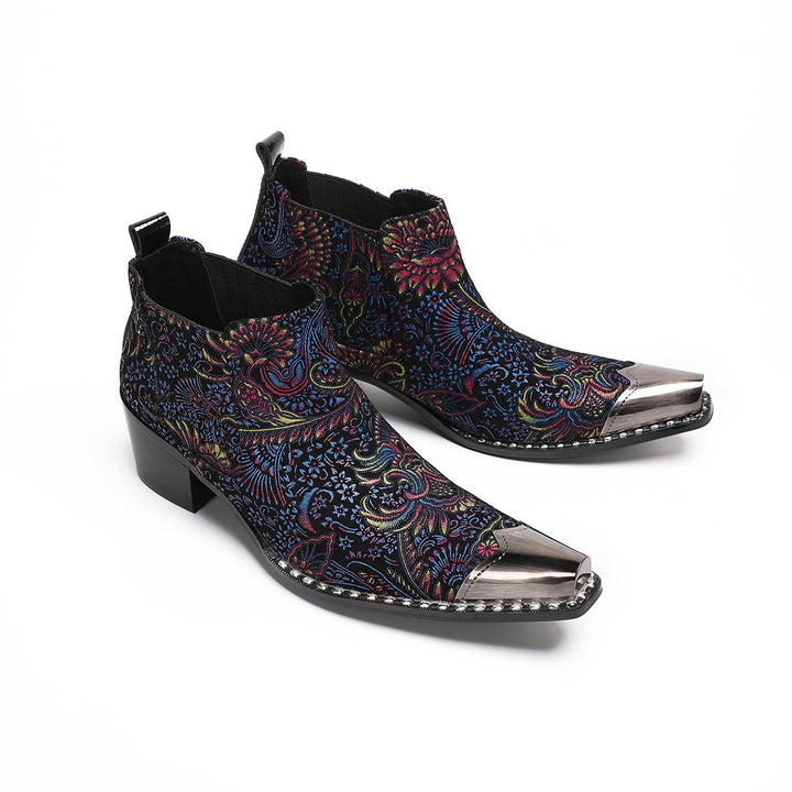 A pair of men's black ankle boots with a vibrant multicolor brocade pattern and a polished silver metal toe cap.