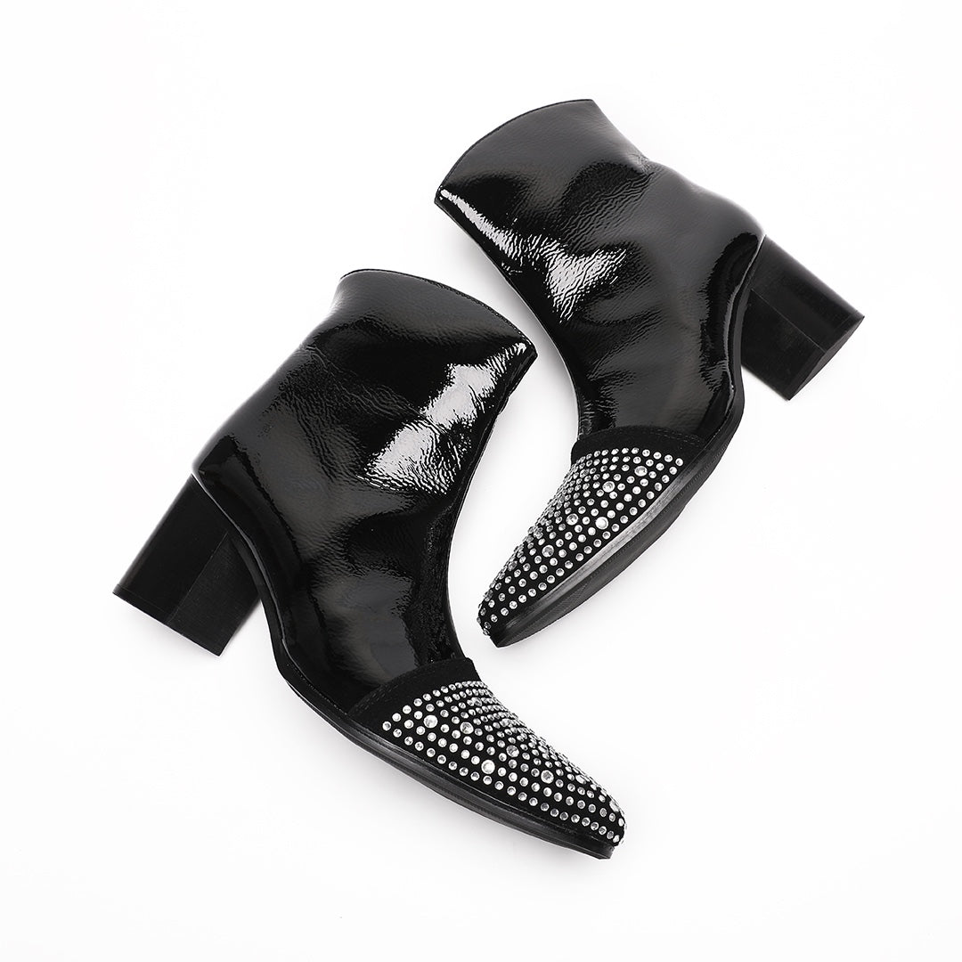 A pair of black patent leather ankle boots with rhinestone-embellished pointed toes and block heels.