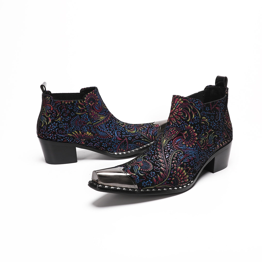 A pair of men's black ankle boots with a vibrant multicolor brocade pattern and a polished silver metal toe cap.