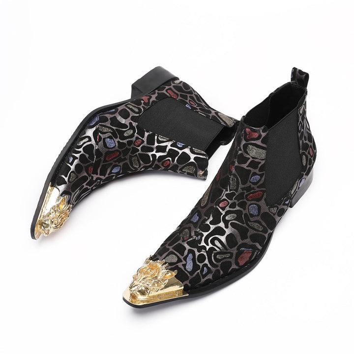 Pair of men's black Chelsea boots with a metallic leopard print pattern and ornate gold metal toe caps, shown on a white